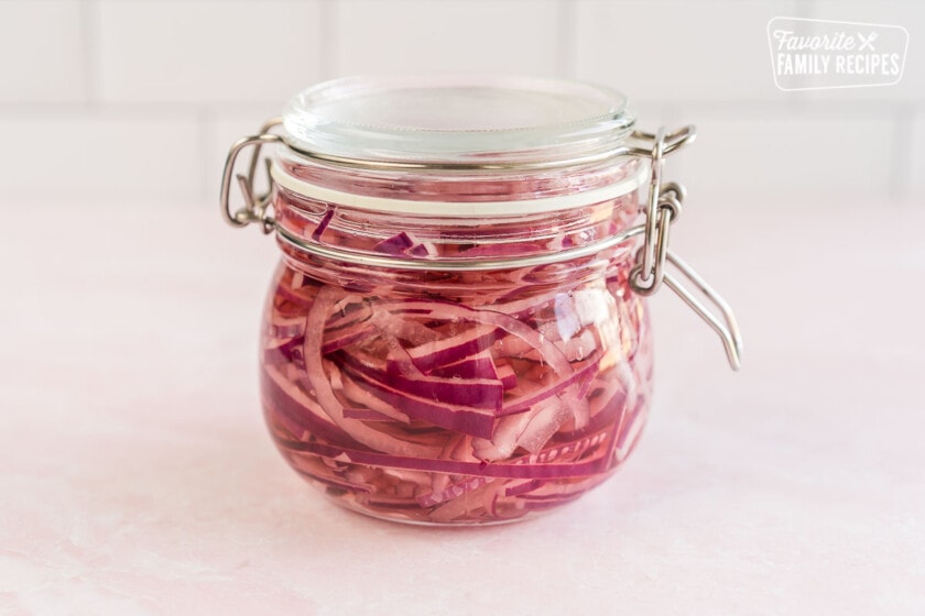 Thinly sliced red onions in a jar full of pickling mixture with a lid