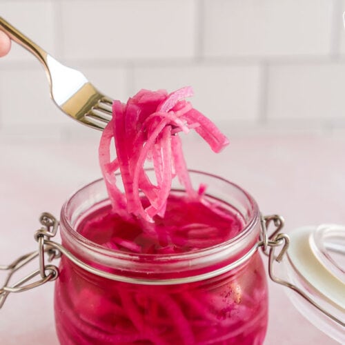 A hand using a fork to scoop some pickled red onions out of a jar