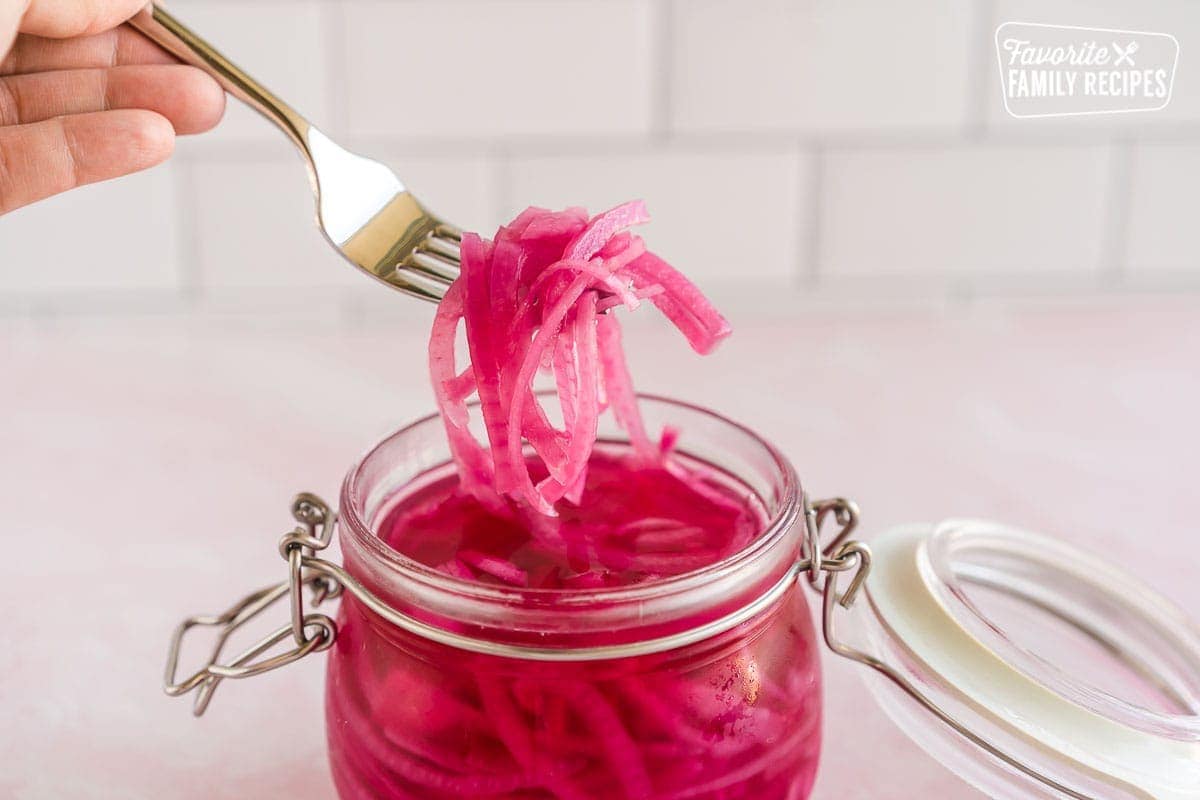 A hand using a fork to scoop some pickled red onions out of a jar.