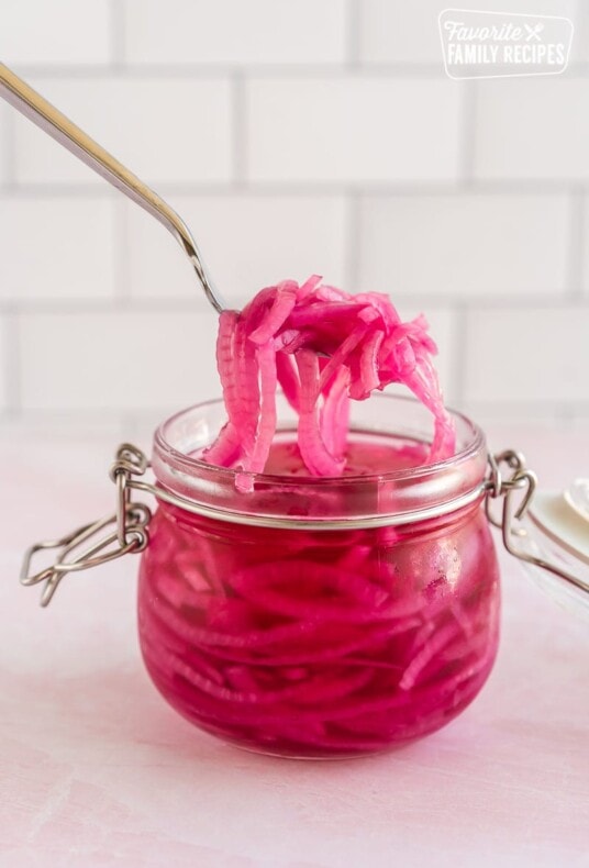 A hand using a fork to scoop some pickled red onions out of a jar