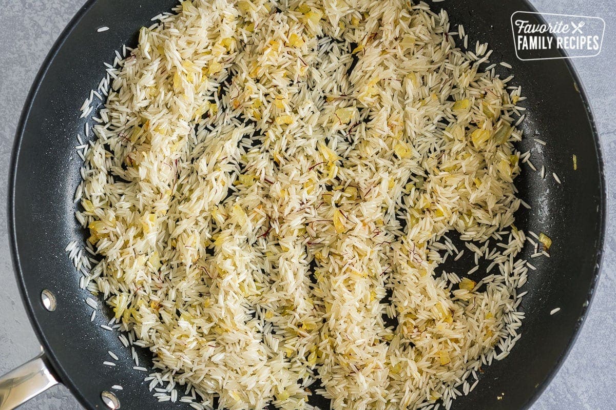 A large pan filled with cooked onions, garlic, and saffron, and uncooked basmati rice