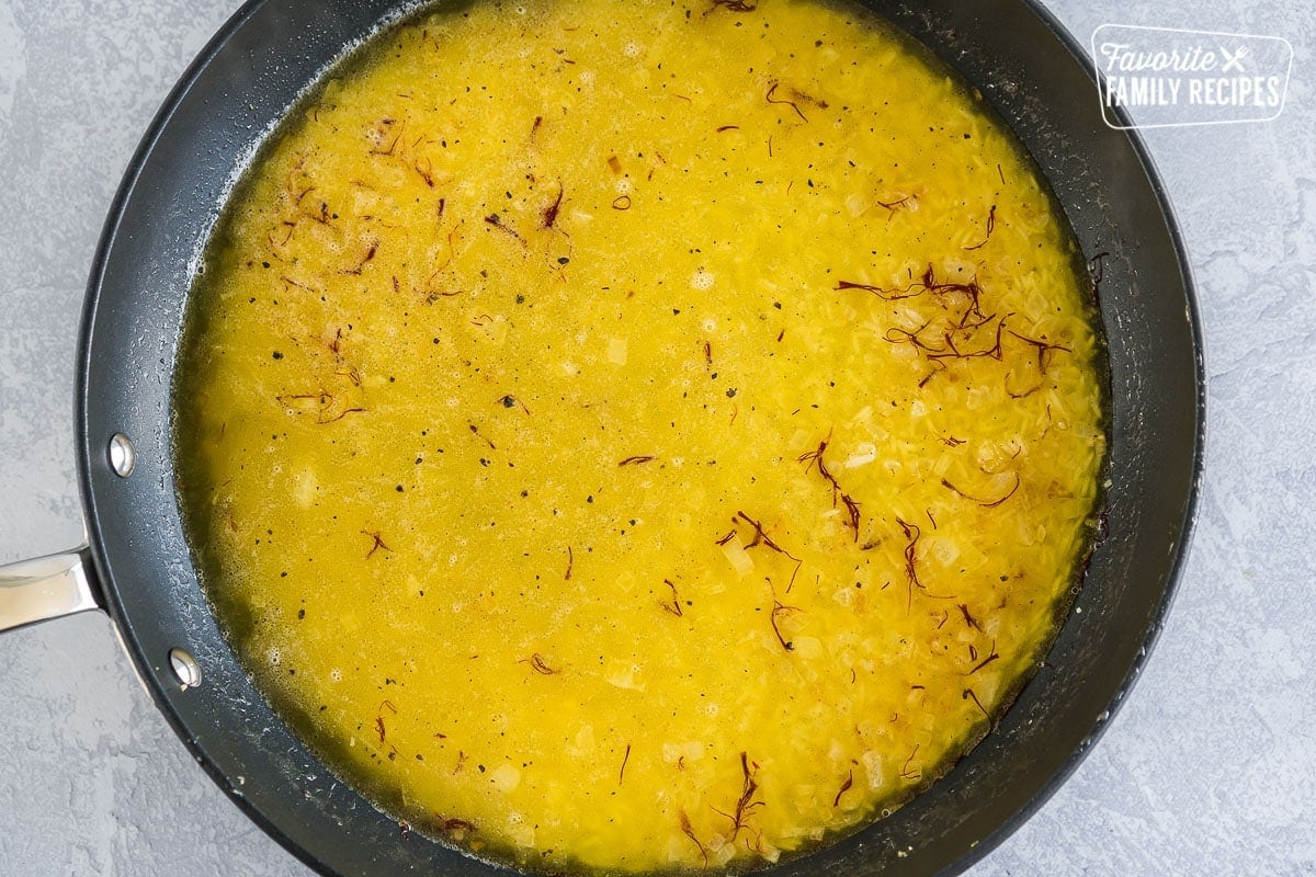 A large skillet filled with basmati rice, saffron, chicken broth, onions, and garlic