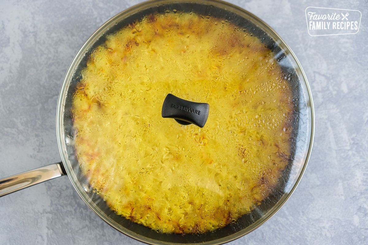 A large skillet with a clear lid. Through the lid you can see yellow rice.