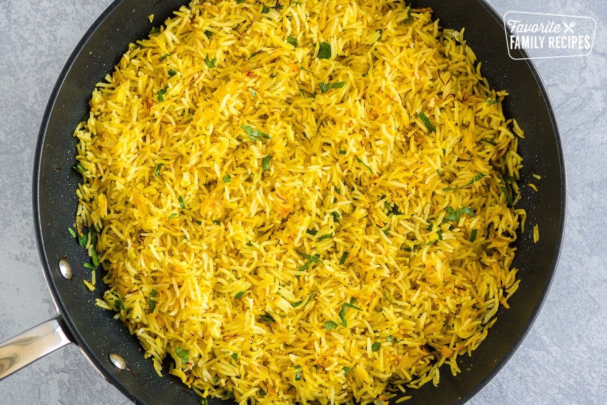 A large skillet filled with yellow saffron rice and topped with chopped parsley