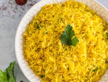 A large bowl of saffron rice topped with a parsley leaf