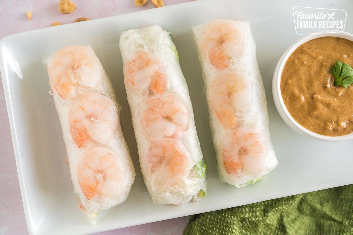 Three Shrimp Spring Rolls on a plate with a bowl of peanut dipping sauce