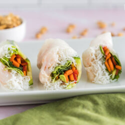 Three Shrimp Spring Rolls cut in half on a plate with a bowl of peanut dipping sauce