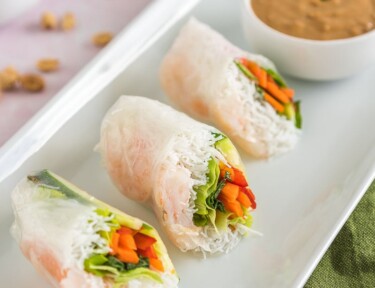 Three Shrimp Spring Rolls cut in half on a plate with a bowl of peanut dipping sauce