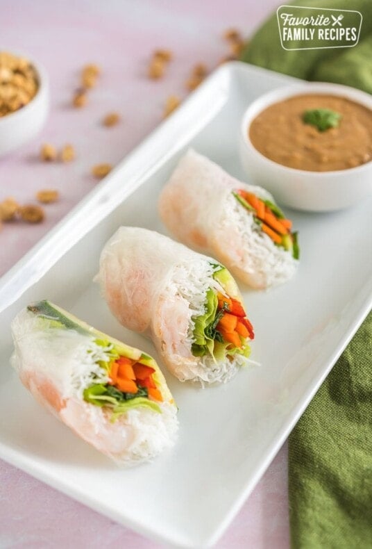 Three Shrimp Spring Rolls cut in half on a plate with a bowl of peanut dipping sauce