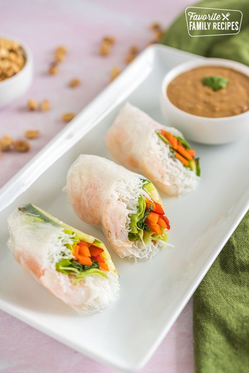 Three Shrimp Spring Rolls cut in half on a plate with a bowl of peanut dipping sauce