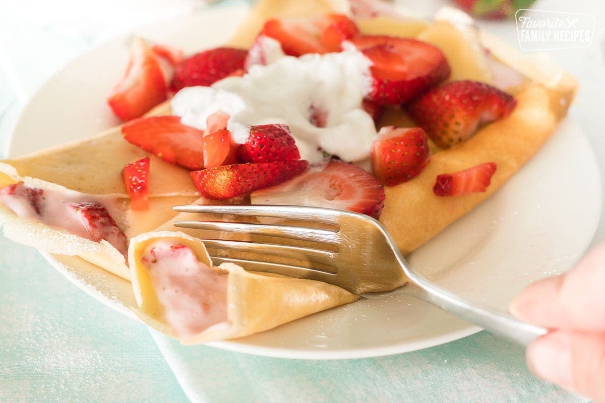 Close up of a fork cutting into a strawberry crepe to show the creamy filling