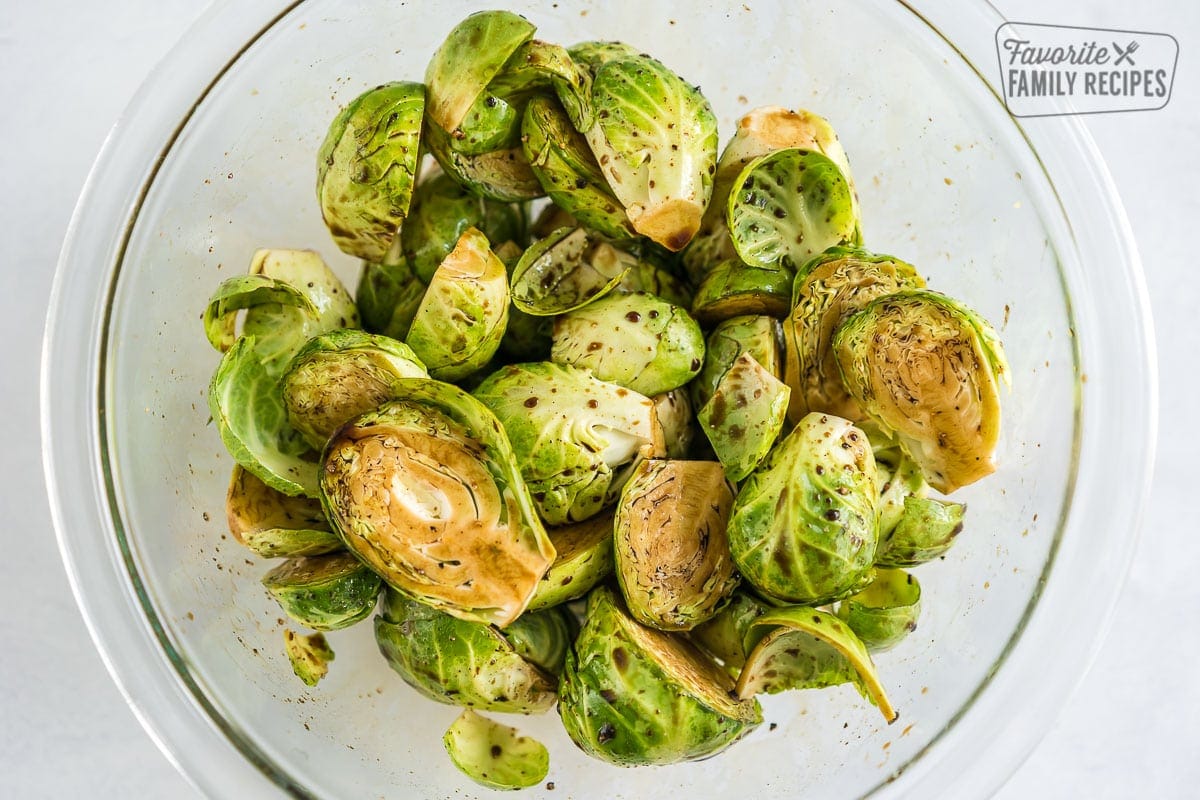 Halved Brussels sprouts in a bowl covered with olive oil and balsamic vinegar