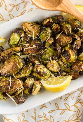 Cooked Brussels Sprouts on a plate with parmesan cheese and lemon wedges