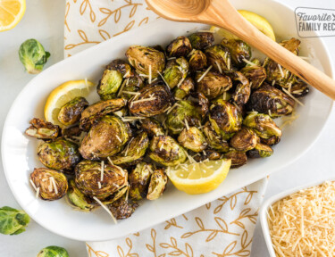 Cooked Brussels Sprouts on a plate with parmesan cheese and lemon wedges