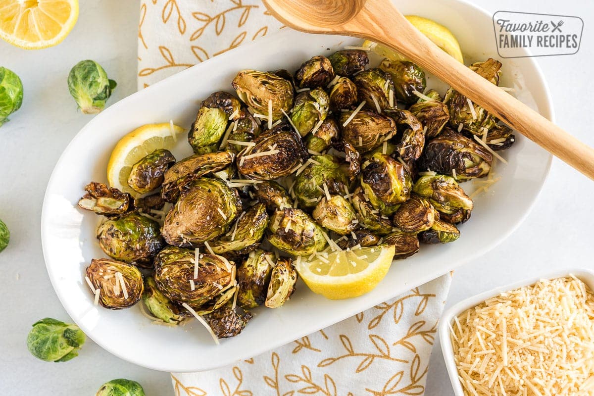 Cooked Brussels Sprouts on a plate with parmesan cheese and lemon wedges.