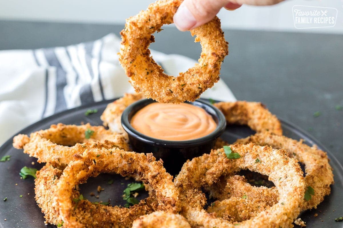 An onion ring made in the air fryer being dipped in sauce