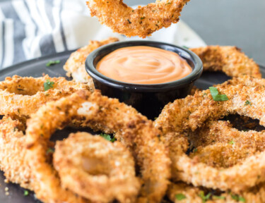 An onion ring made in the air fryer being dipped in sauce