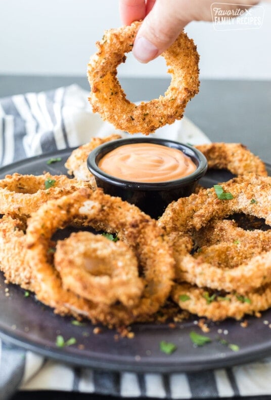 An onion ring made in the air fryer being dipped in sauce