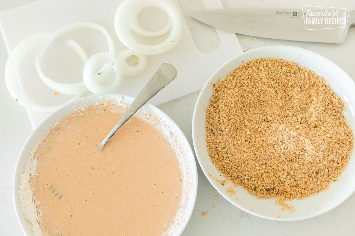 Sliced onions, a bowl of batter, and a bowl of breadcrumbs