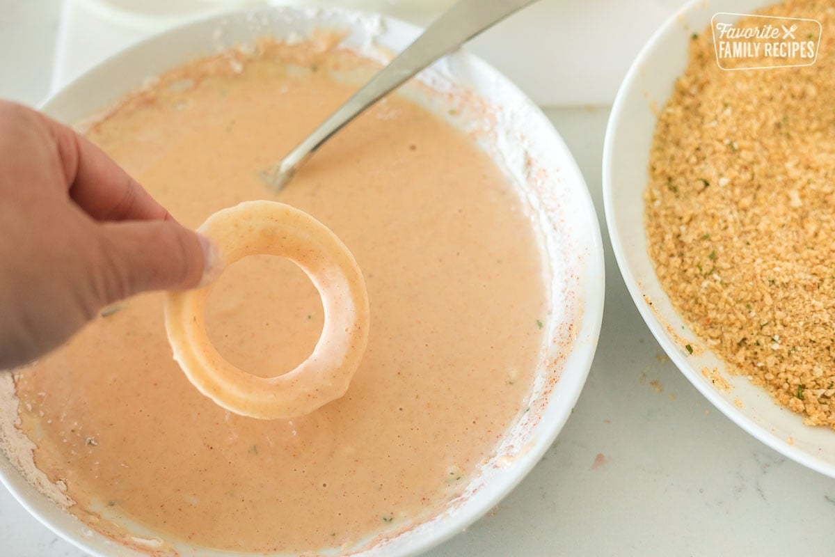 An onion ring being dipped in batter