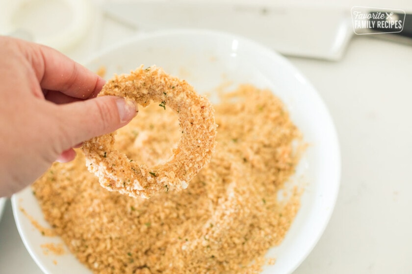 An onion ring being dipped in breadcrumbs before air frying