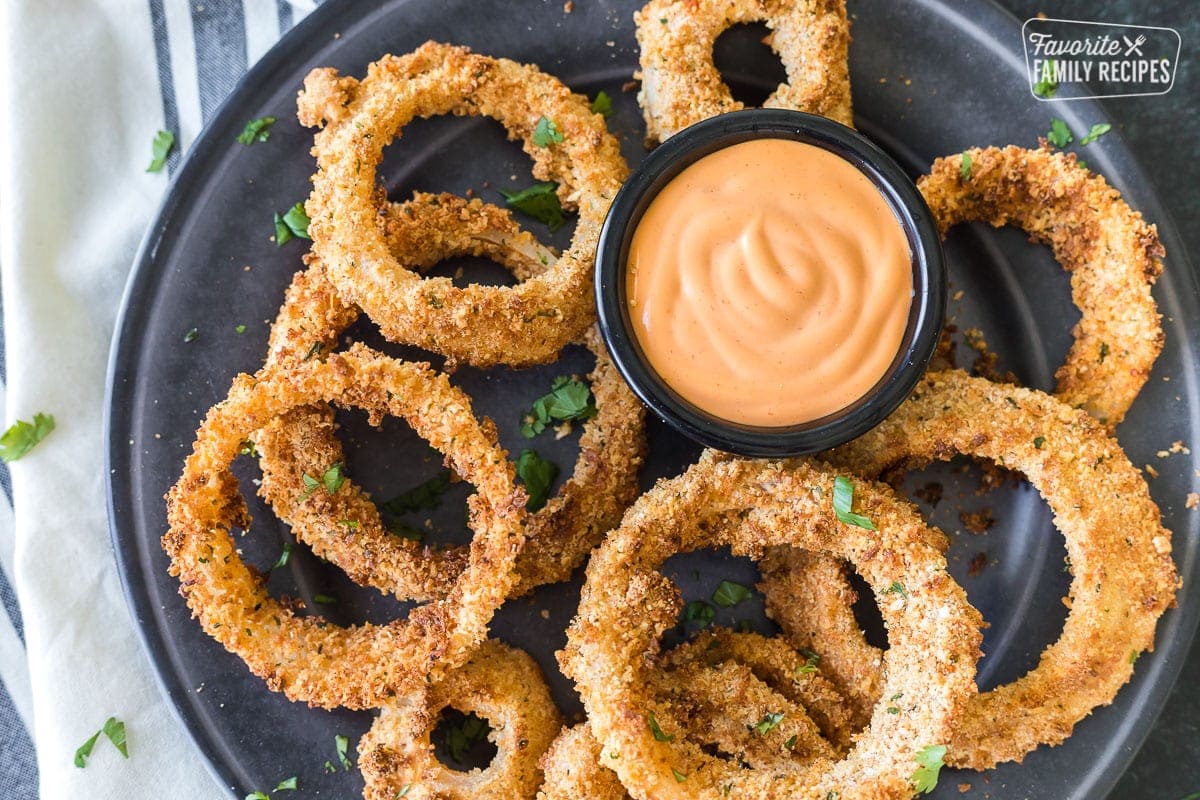 Top view of a plate of air fryer onion rings with a cup of sauce