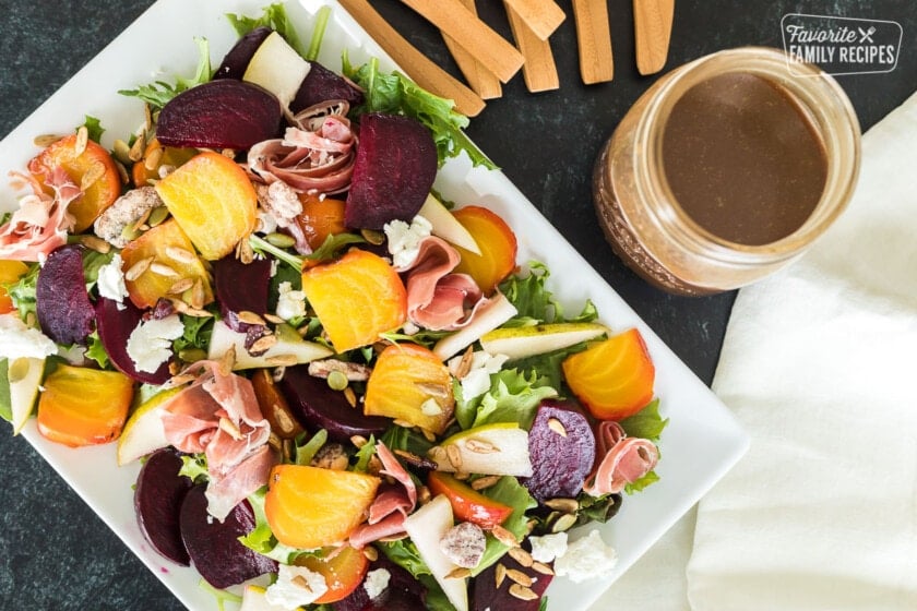 Top view of a beet salad with toppings next to a jar of homemade balsamic vinaigrette