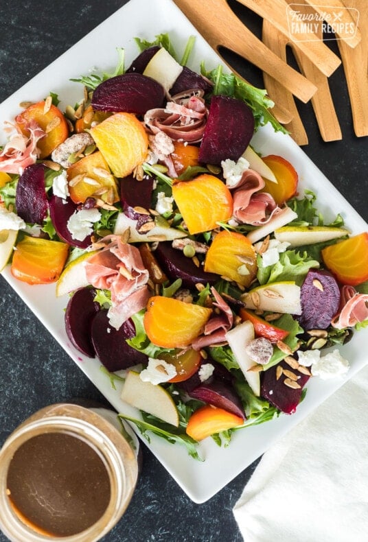 Top view of a beet salad with toppings next to a jar of homemade balsamic vinaigrette