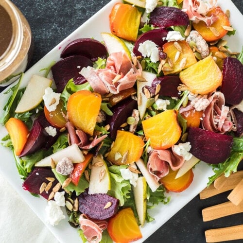 Top view of a beet salad with toppings next to a jar of homemade balsamic vinaigrette