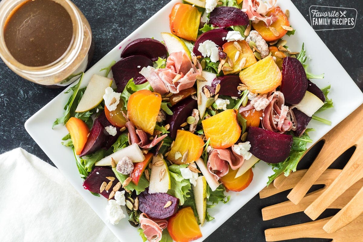 Top view of a beet salad with toppings next to a jar of homemade balsamic vinaigrette.