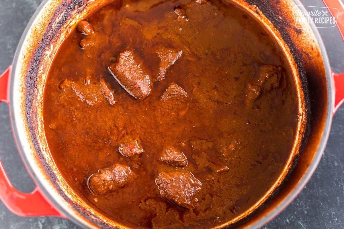 Braised beef in a red sauce to make birria in a large Dutch oven