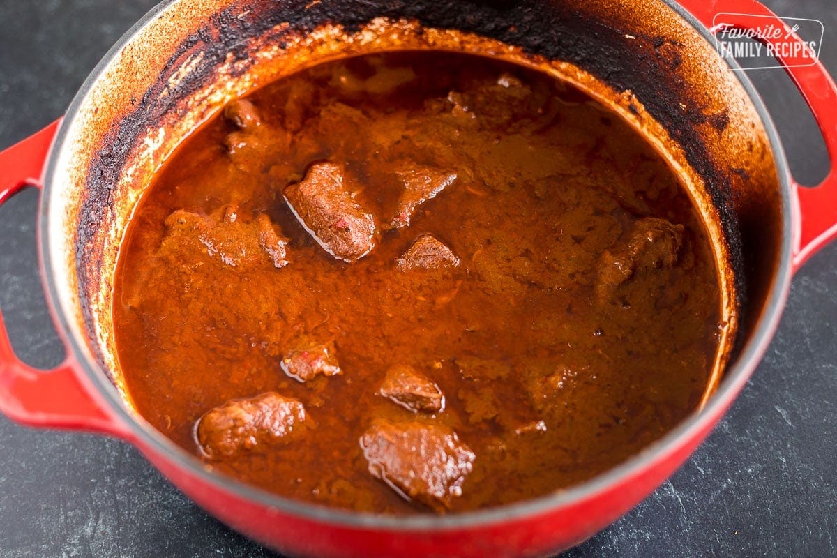 Braised beef in a red sauce to make birria in a large Dutch oven