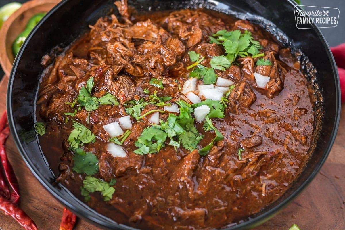 Beef birria in a black serving bowl topped with onions and cilantro