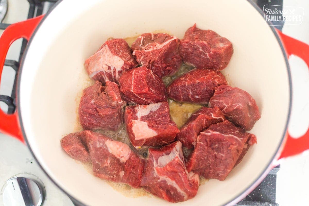 Chunks of uncooked meat in a large Dutch oven being cooked to make birria