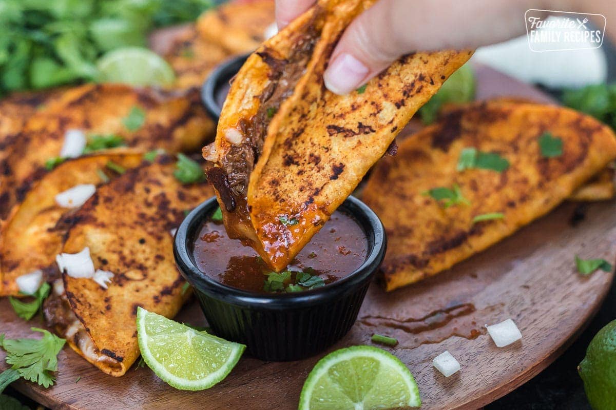 A birria taco being dipped into the birria dip (consommé)