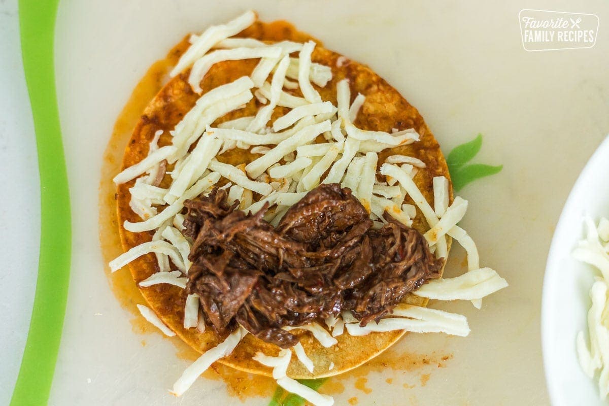 An open-face birria taco with shredded cheese and shredded birria beef showing