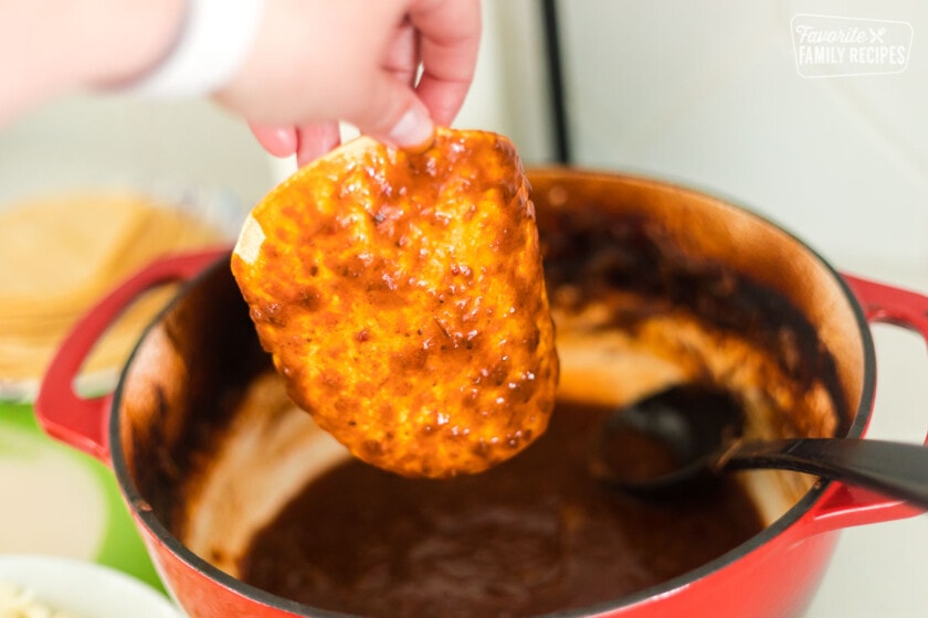 A corn tortilla being dipped in the birria sauce.