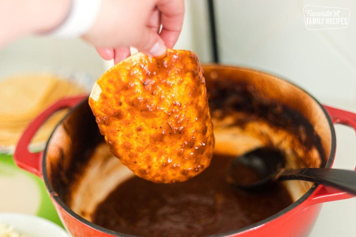 A corn tortilla being dipped in the birria sauce