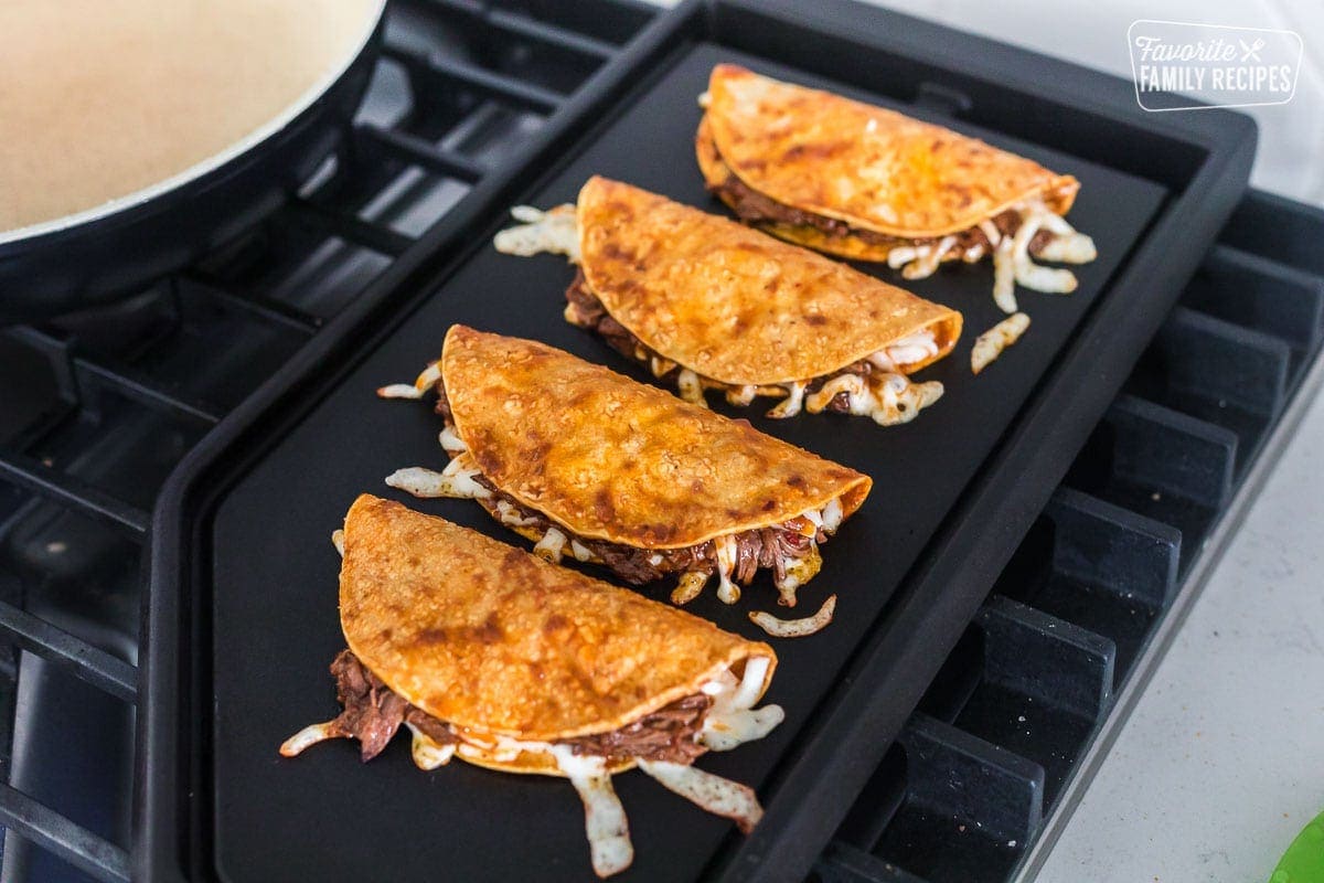 Birria tacos on a griddle with beef and cheese showing