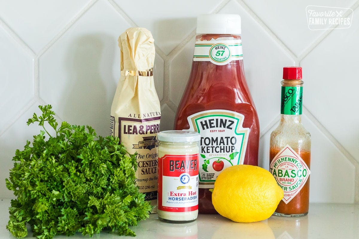 Ingredients to make cocktail sauce including ketchup, horseradish, tabasco, lemon, Worcestershire sauce, and parsley