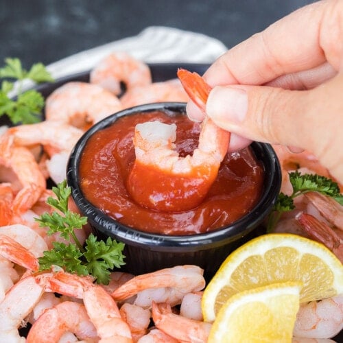 A shrimp being dipped into cocktail sauce