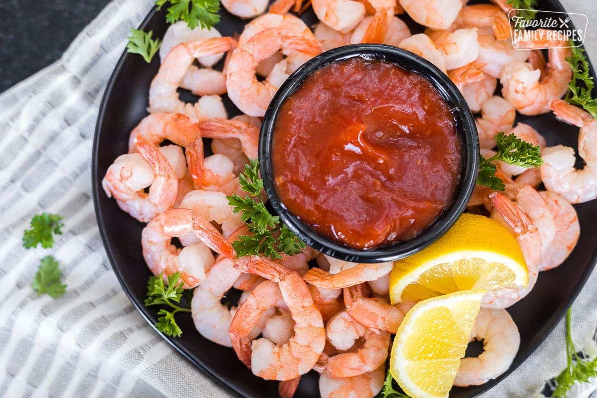 A platter of cocktail shrimp with a cup of cocktail sauce