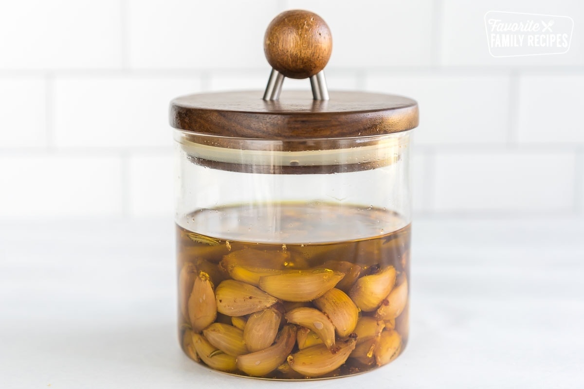 Garlic confit in a glass jar with a wooden lid.