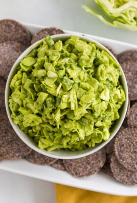 A bowl of green goddess dip on a plate of blue corn chips