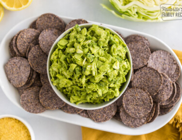 A bowl of green goddess dip on a plate of blue corn chips