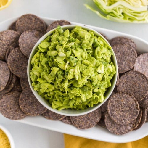 A bowl of green goddess dip on a plate of blue corn chips