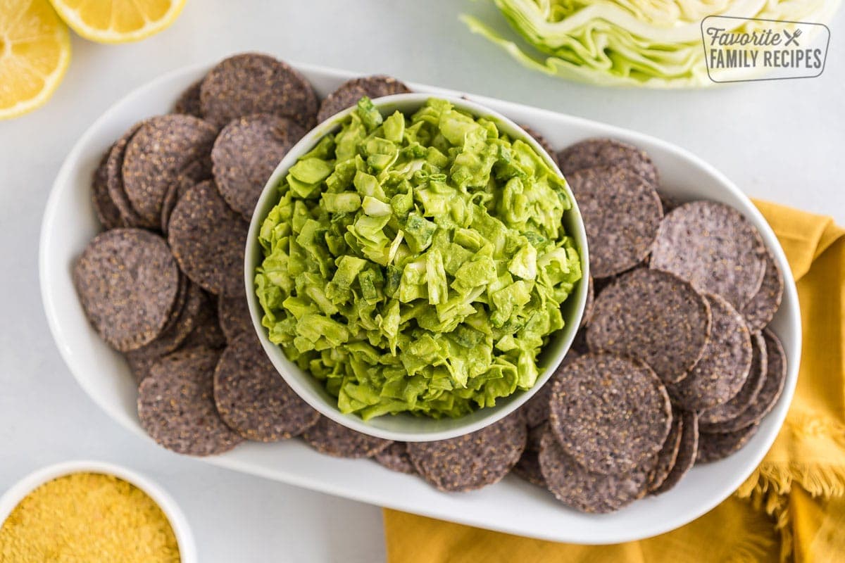A bowl of green goddess dip on a plate of blue corn chips.