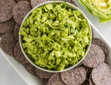 A bowl of green goddess dip on a plate of blue corn chips