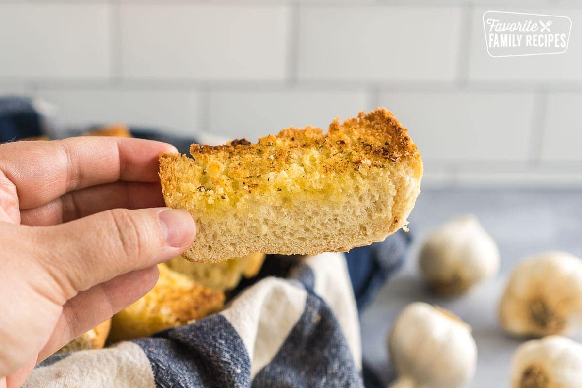 A hand holding up a slice of garlic bread.