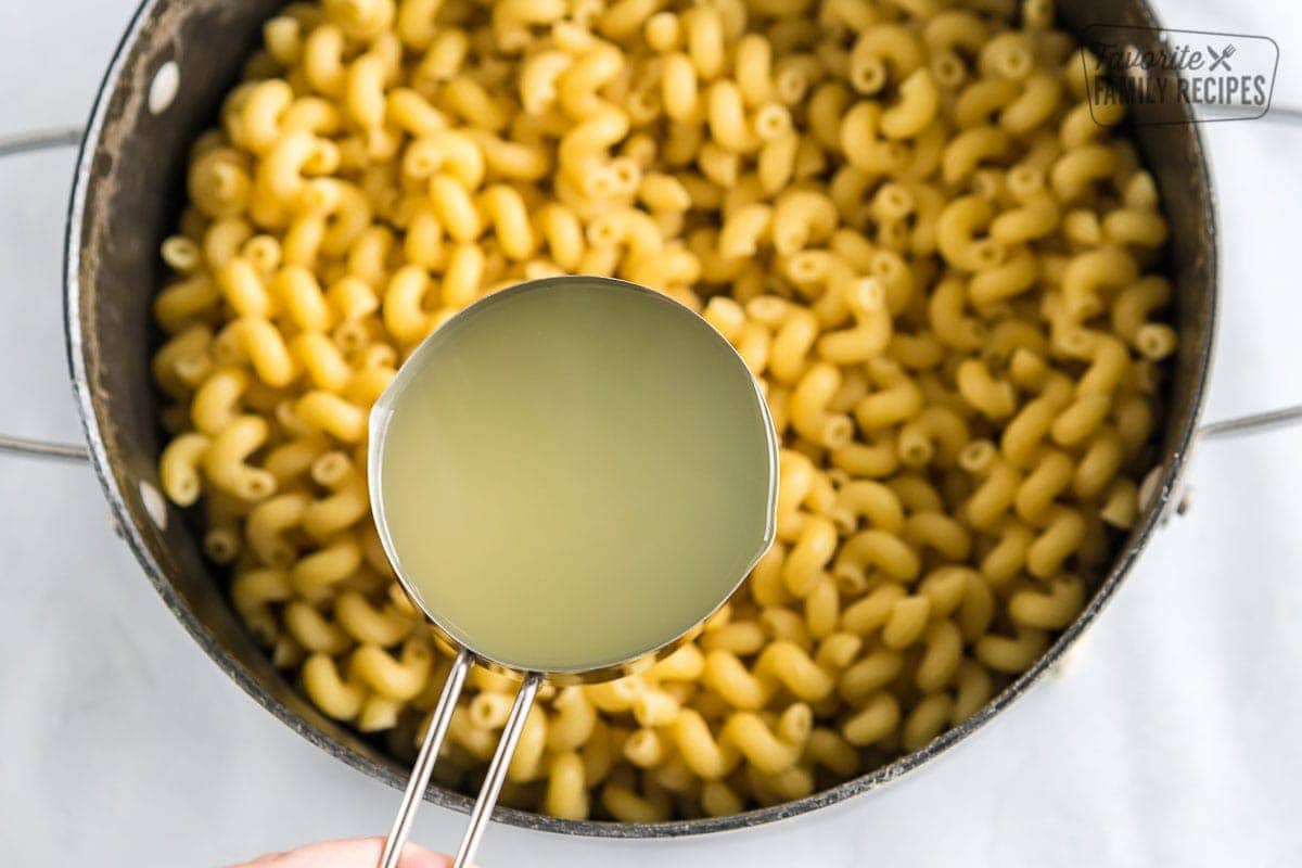 A measuring cup full of pasta water held over a pot of pasta